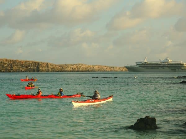 GUESTS KAYAKING AT DARWIN BAY GENOVESA ISLAND WITH THE SILVER ORIGIN ON THE BACKGROUND